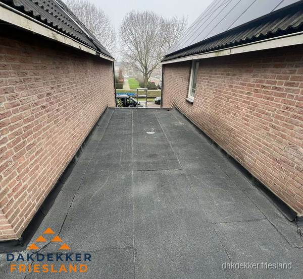 Plat dak met bitumen dakbedekking tussen bakstenen muren in Friesland