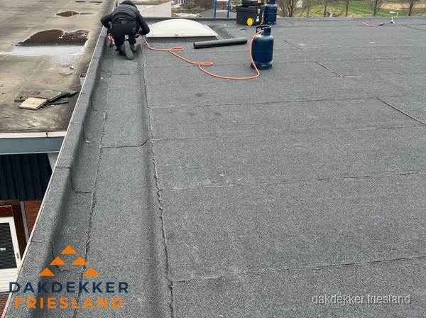 Dakdekker repareert bitumen dakbedekking op groot plat dak in Friesland